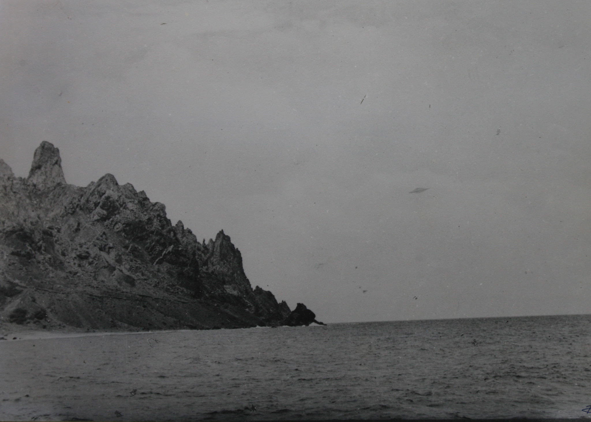 Auf einem schwarz-weiß Foto ist Wasser und eine Küste abgebildet. Im Himmel sind Schlieren zu sehen, die mit viel Fantasie ein Unbekanntes Flugobjekt sein könnten.